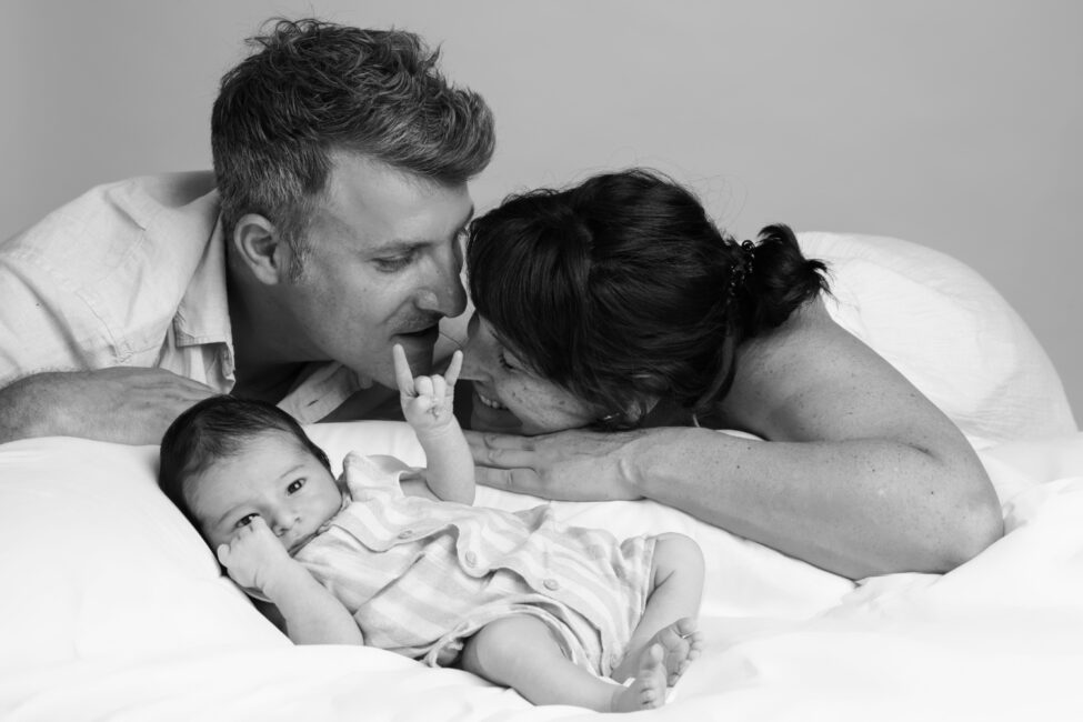 Portrait de famille en noir et blanc avec un nouveau-né et derrière-lui ses parents lors d’une séance photo