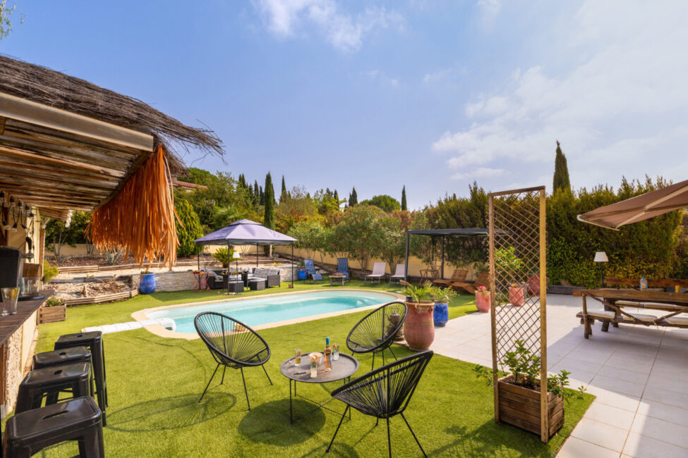 Jardin aménagé autour de la piscine avec fauteuils, table basse, transats, tonnelle, terrasse et espace bar extérieur.
