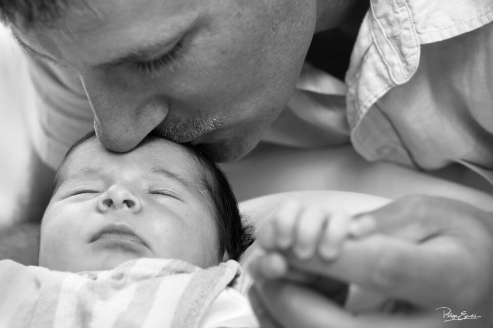 Moment de tendresse entre un papa qui pose ses lèvres sur le front de son nouveau-né photographié en noir et blanc