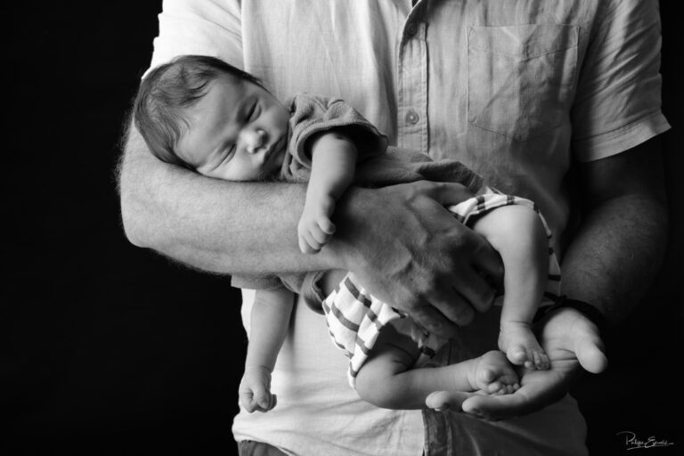 Nouveau-né paisiblement installé dans les bras de son papa en photographie noir et blanc.