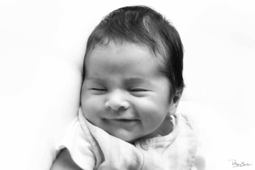 Portrait en noir et blanc d’un nouveau-né souriant lors d’une séance photo bébé.