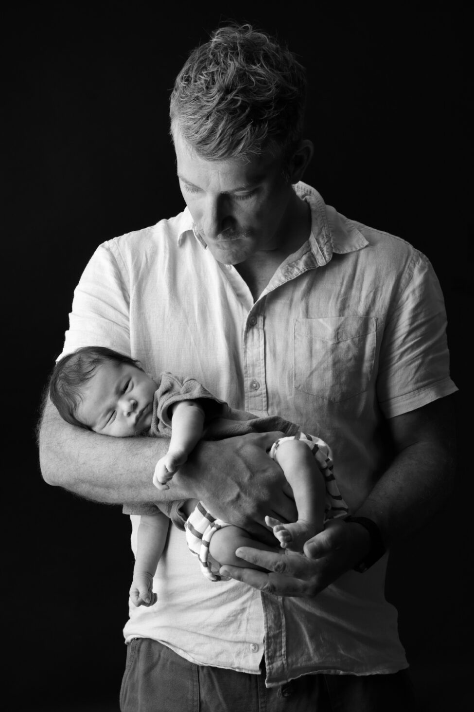 Papa tenant son nouveau-né dans ses bras lors d’une séance photo en noir et blanc