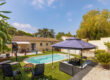 Vue d’ensemble de la piscine et du jardin avec salon extérieur sous tonnelle, transats et maison en arrière-plan.