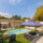 Vue d’ensemble de la piscine et du jardin avec salon extérieur sous tonnelle, transats et maison en arrière-plan.