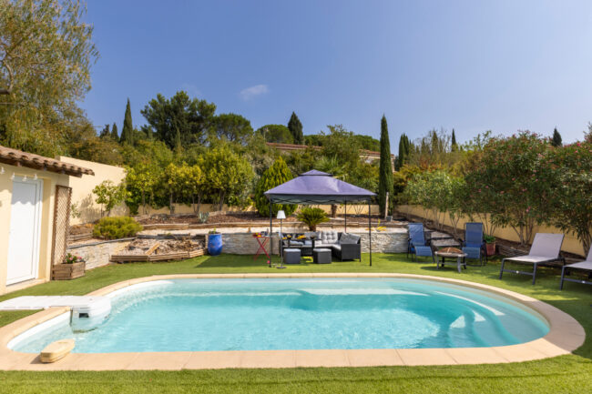 Piscine extérieure entourée d’un jardin aménagé avec salon sous tonnelle, transats, végétation méditerranéenne et espaces de détente.
