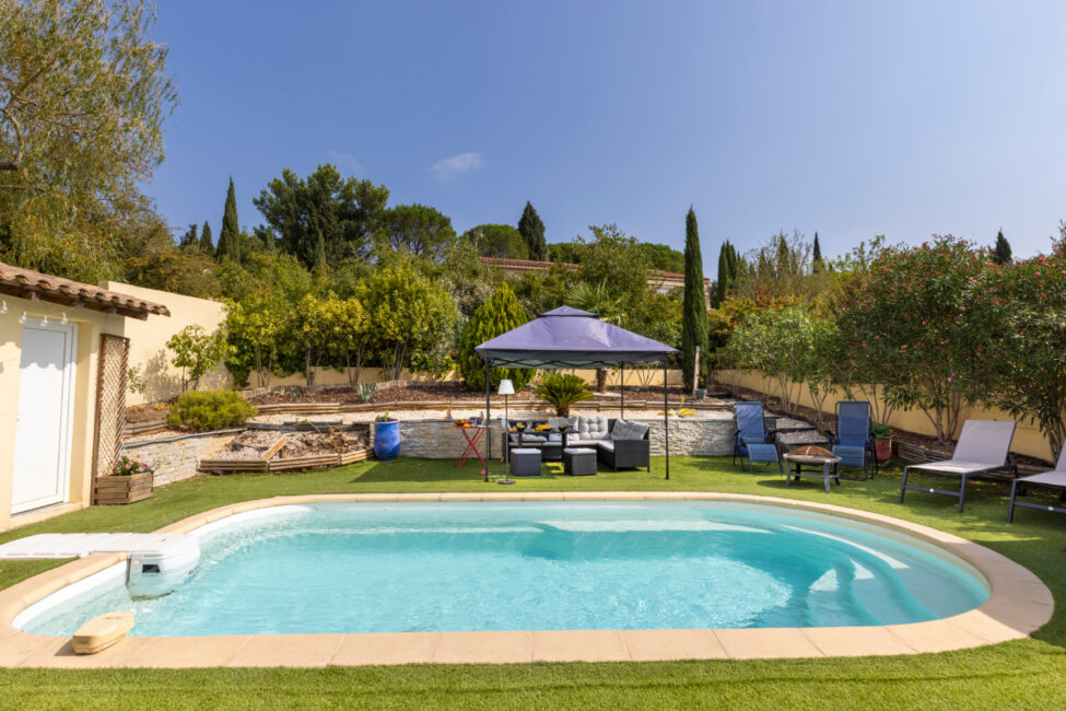 Piscine extérieure entourée d’un jardin aménagé avec salon sous tonnelle, transats, végétation méditerranéenne et espaces de détente.