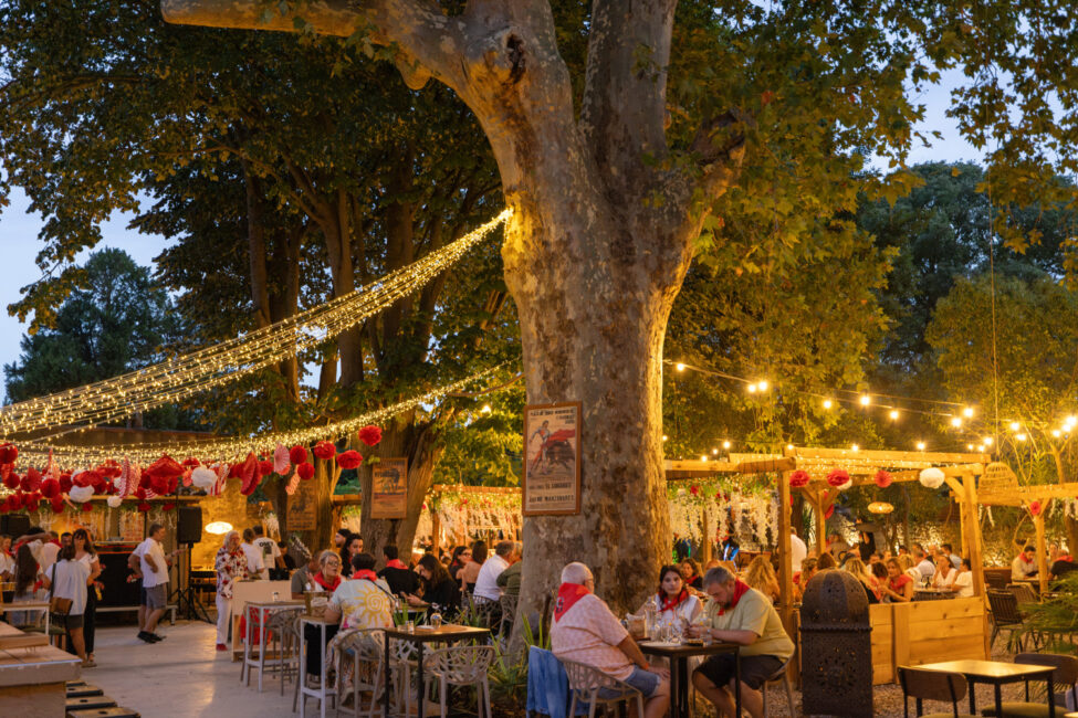 Les Noy’s et le Coco Bongo au cœur de la Féria de Carcassonne 5 Cours de restaurant en plein air à la tombée de nuit, décoration Feria avec affiches de corrida et des lampions accrochés sur les pergolas avec des personnes attablées.
