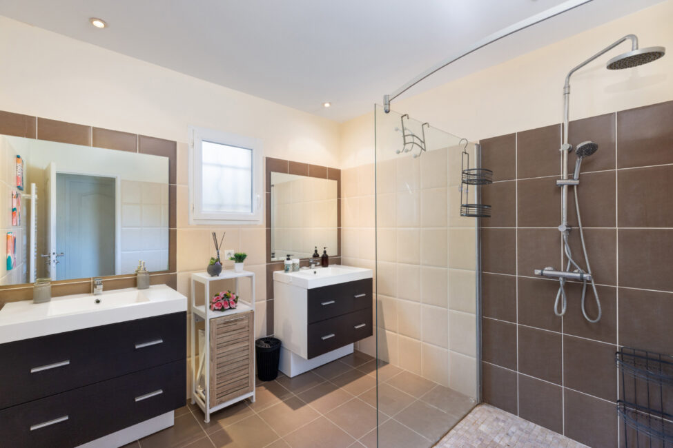 Salle de bain spacieuse avec deux vasques, grands miroirs et douche à l’italienne ouverte avec paroi vitrée.