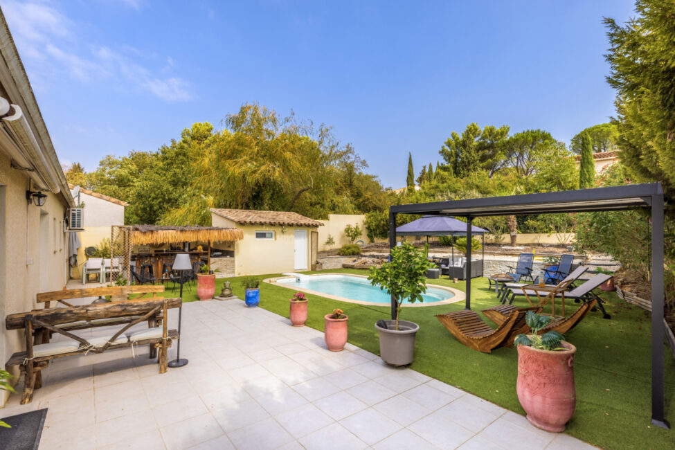 Vue d’ensemble de la terrasse et du jardin avec piscine, pergola, transats en bois, espace bar, mobilier extérieur et végétation arborée.