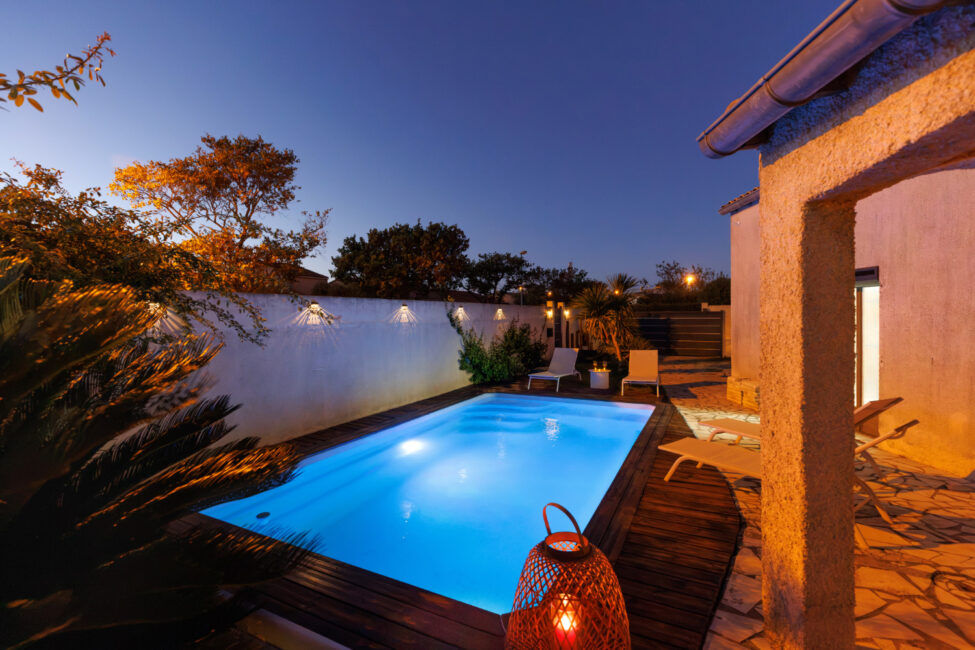À la tombée du jour, les éclairages de la piscine et du jardin révèlent une ambiance paisible, entre lumière bleue du bassin et tons chauds de la terrasse.