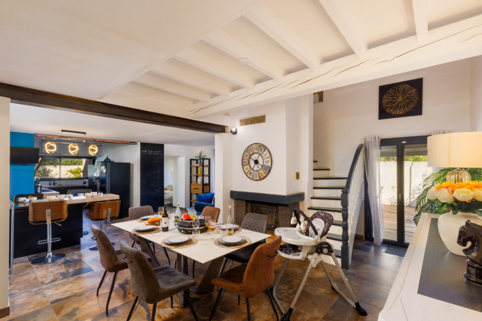 Une pièce de vie conviviale réunissant une grande table à manger, une cuisine ouverte avec comptoir et des poutres apparentes.